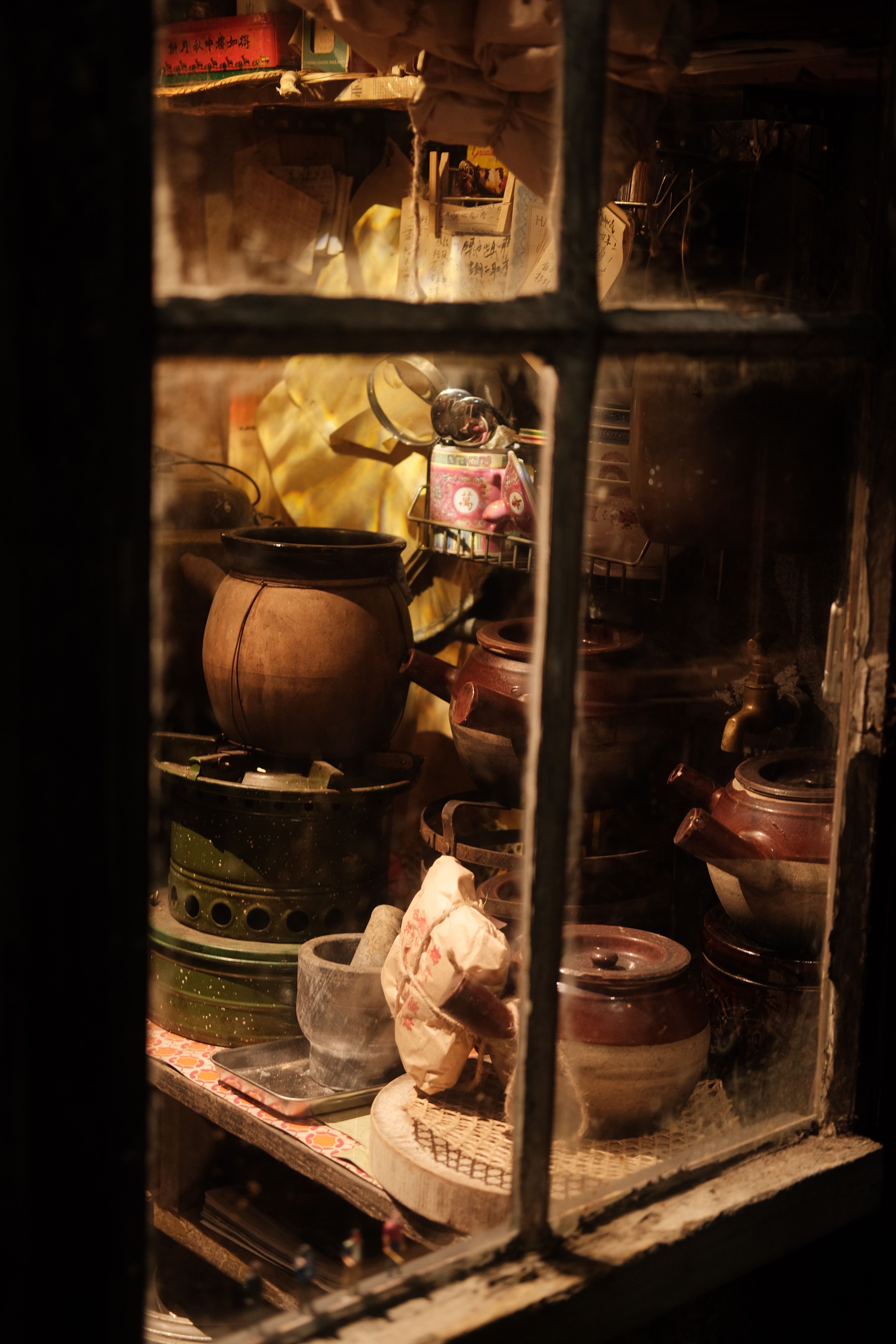 Warmly lit rustic kitchen through an old window, showcasing vintage pots and utensils.