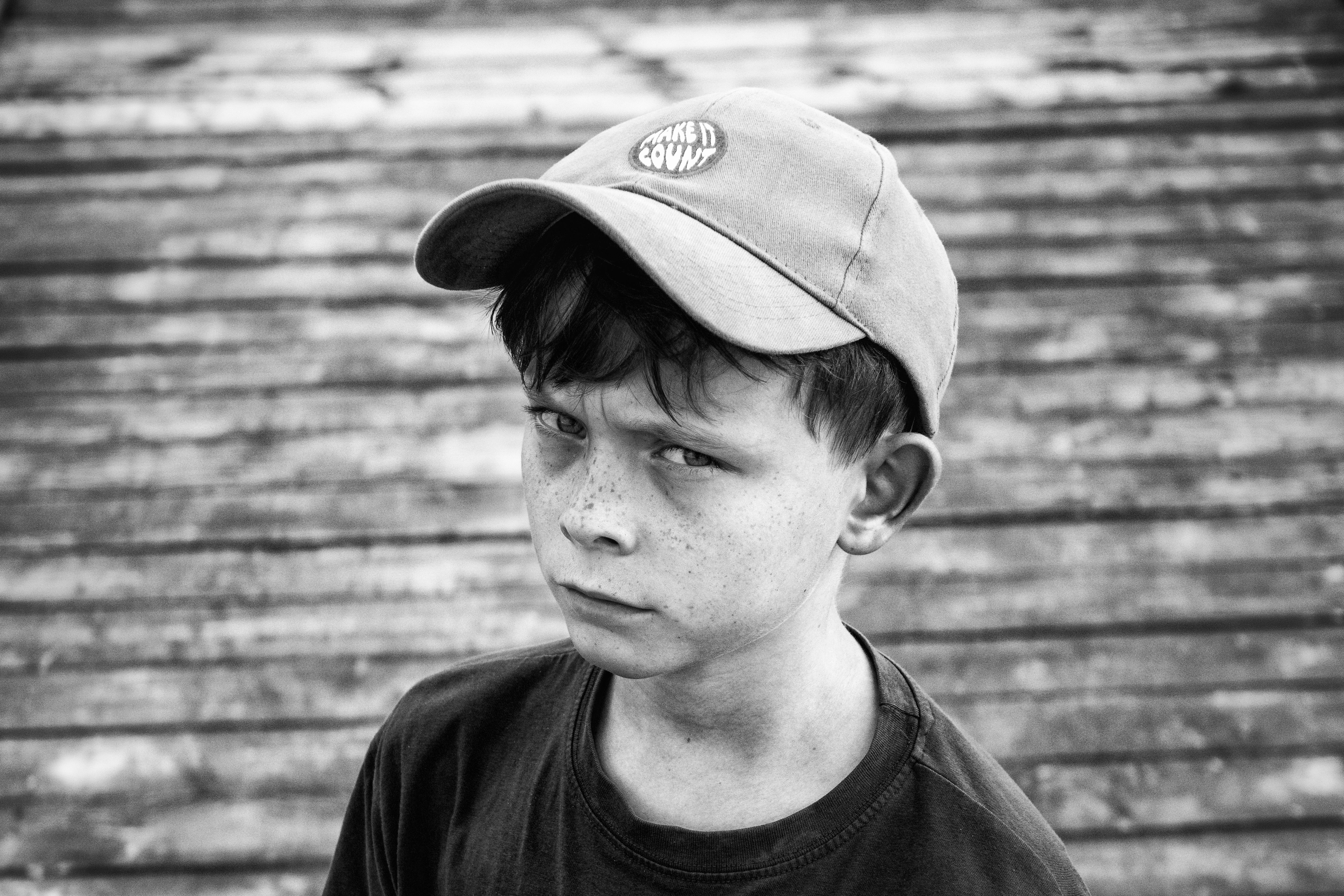 Black and white portrait of a young boy with a cap and freckles, looking serious.