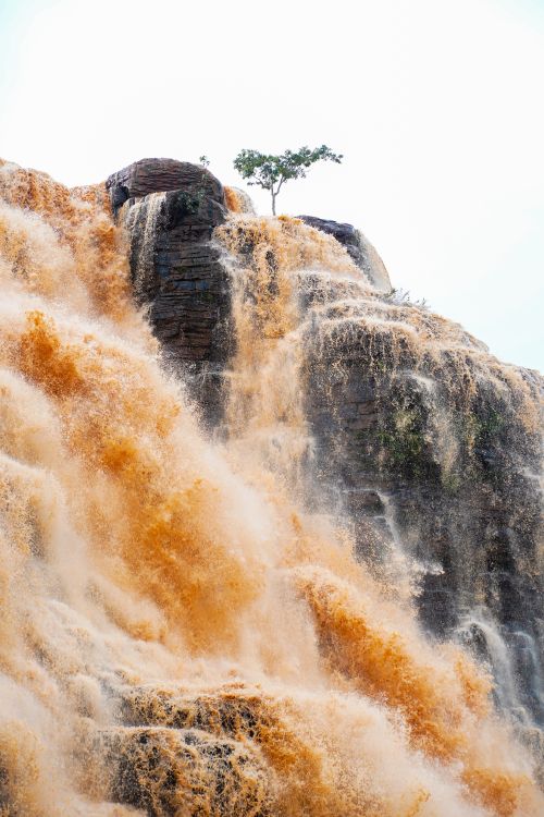 Free Dramatic view of a powerful waterfall with brown water cascading down rocky cliffs. Stock Photo