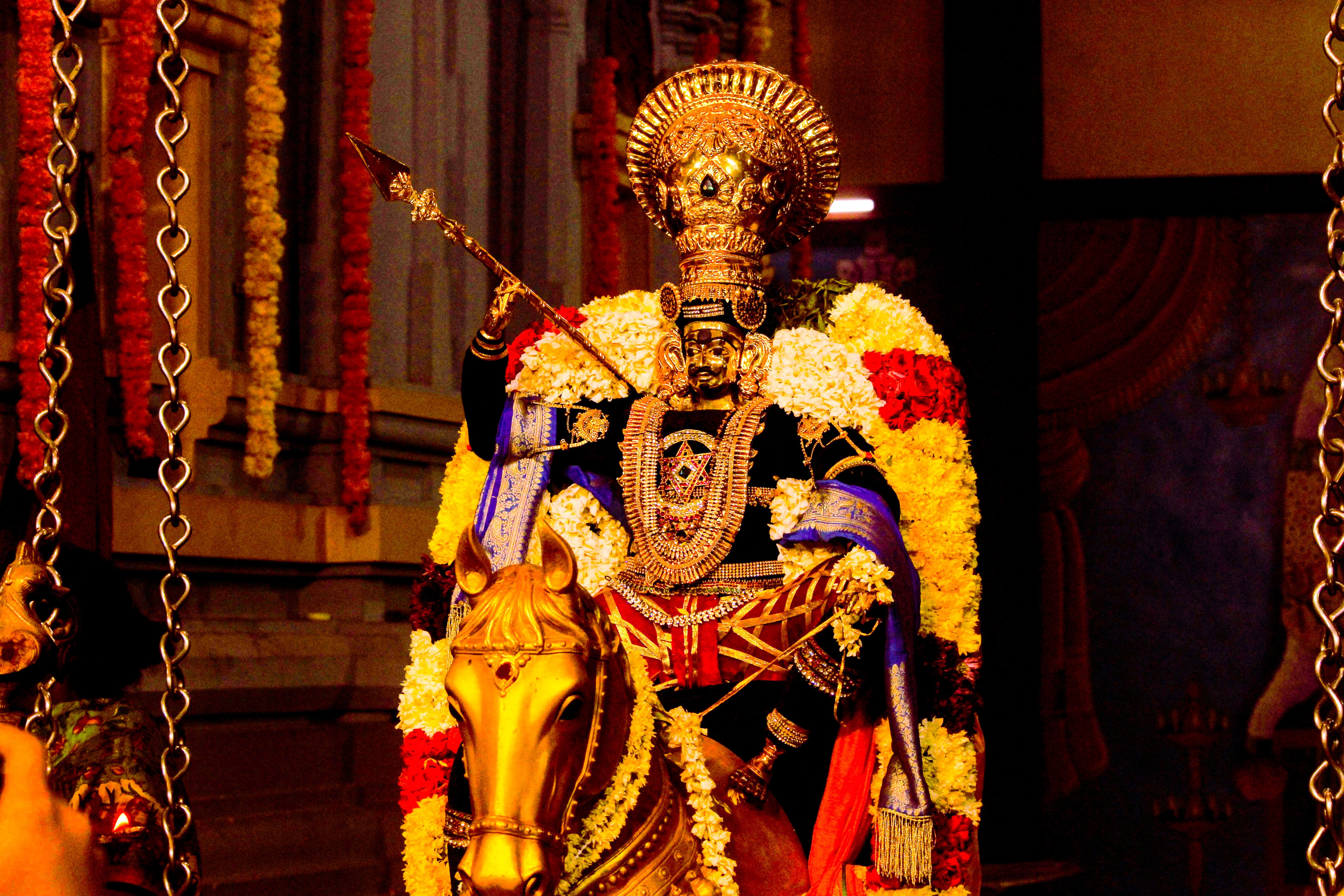 Intricately designed Hindu deity statue lavishly decorated with vibrant flowers and gold accessories indoors.