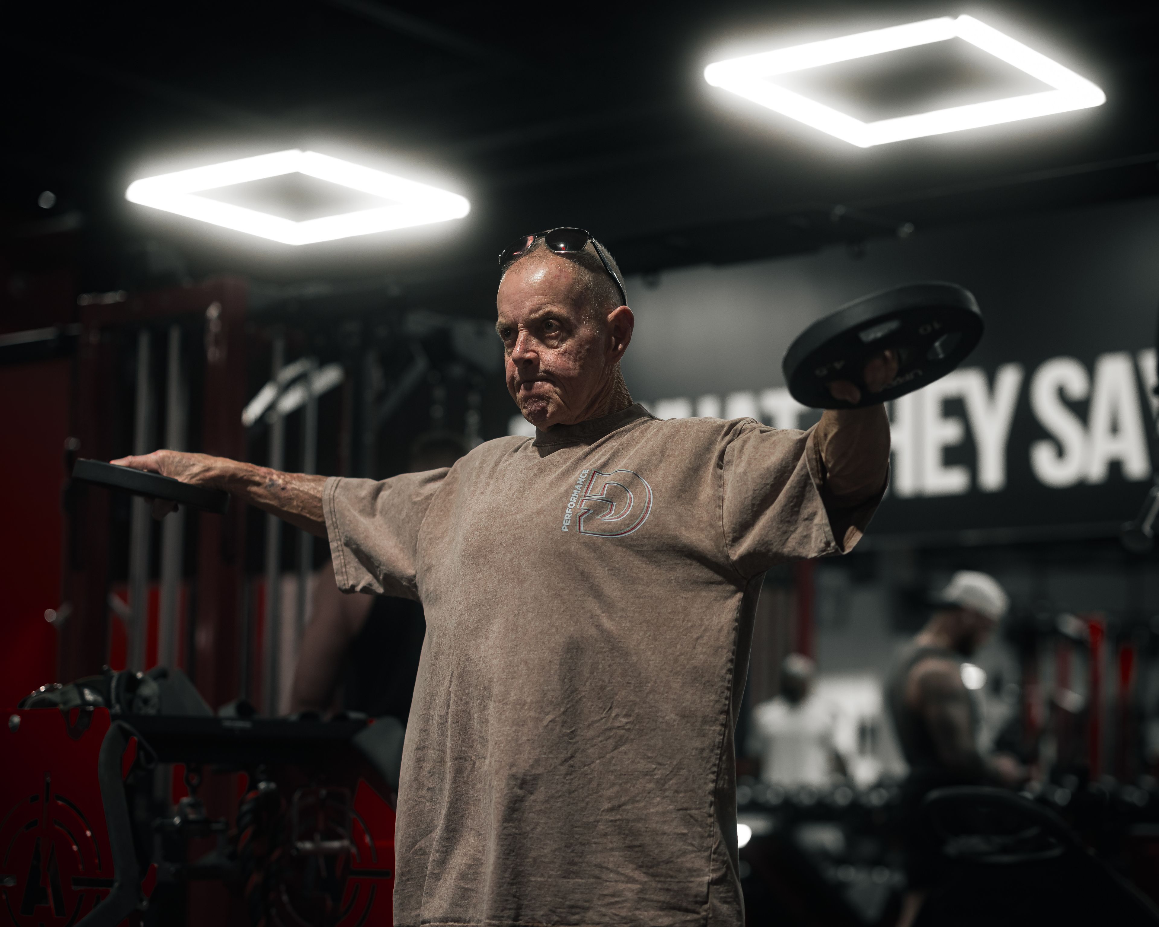 A senior man performs weightlifting exercises inside a dimly lit gym.