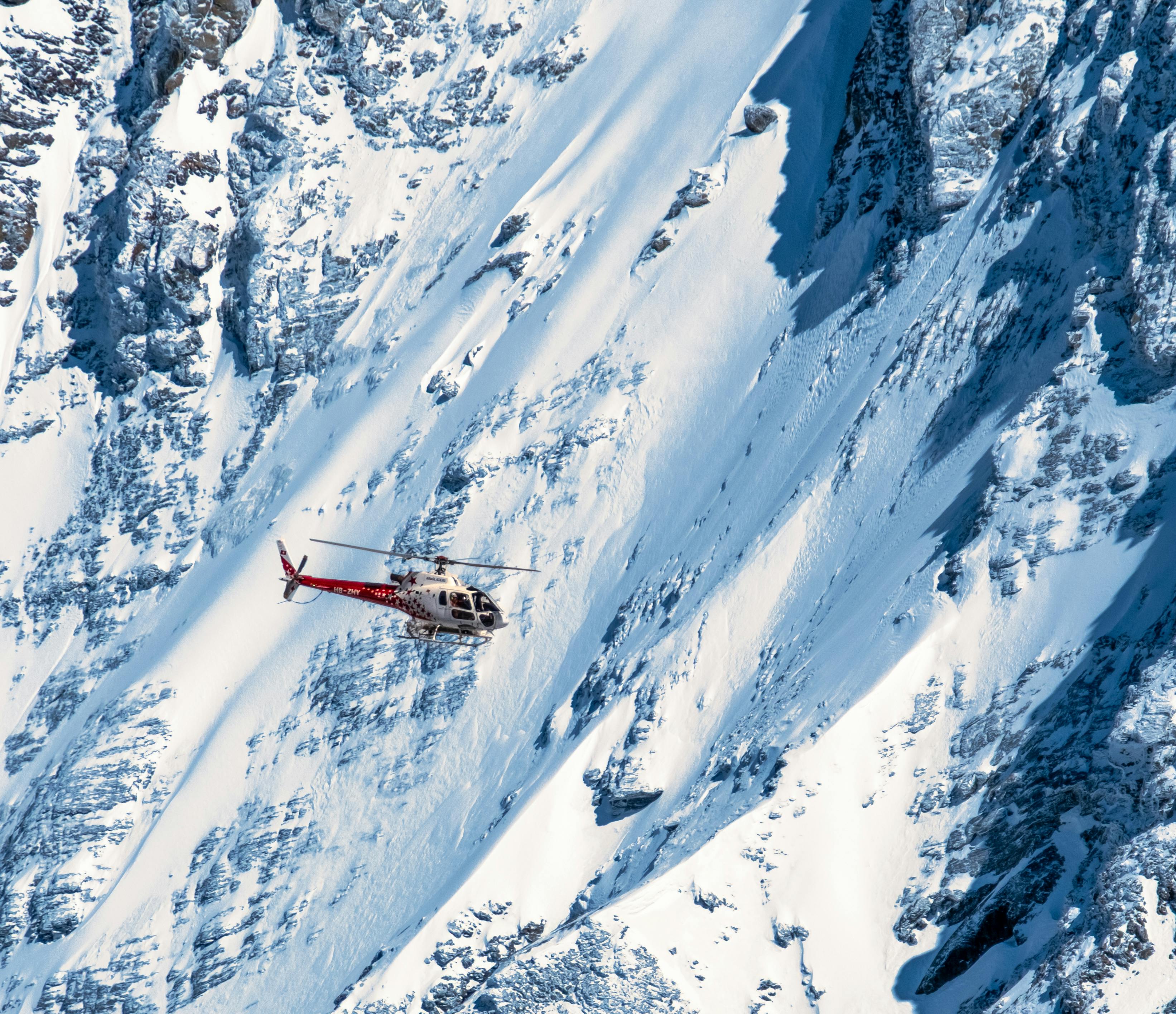 A helicopter soars above the snowy peaks of the Swiss Alps, showcasing winter beauty.