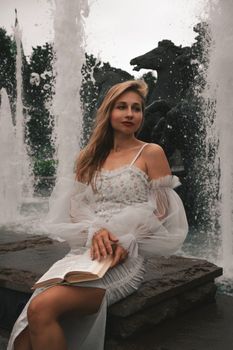 Young woman elegantly reading a book by a beautiful fountain. Captivating and serene atmosphere.