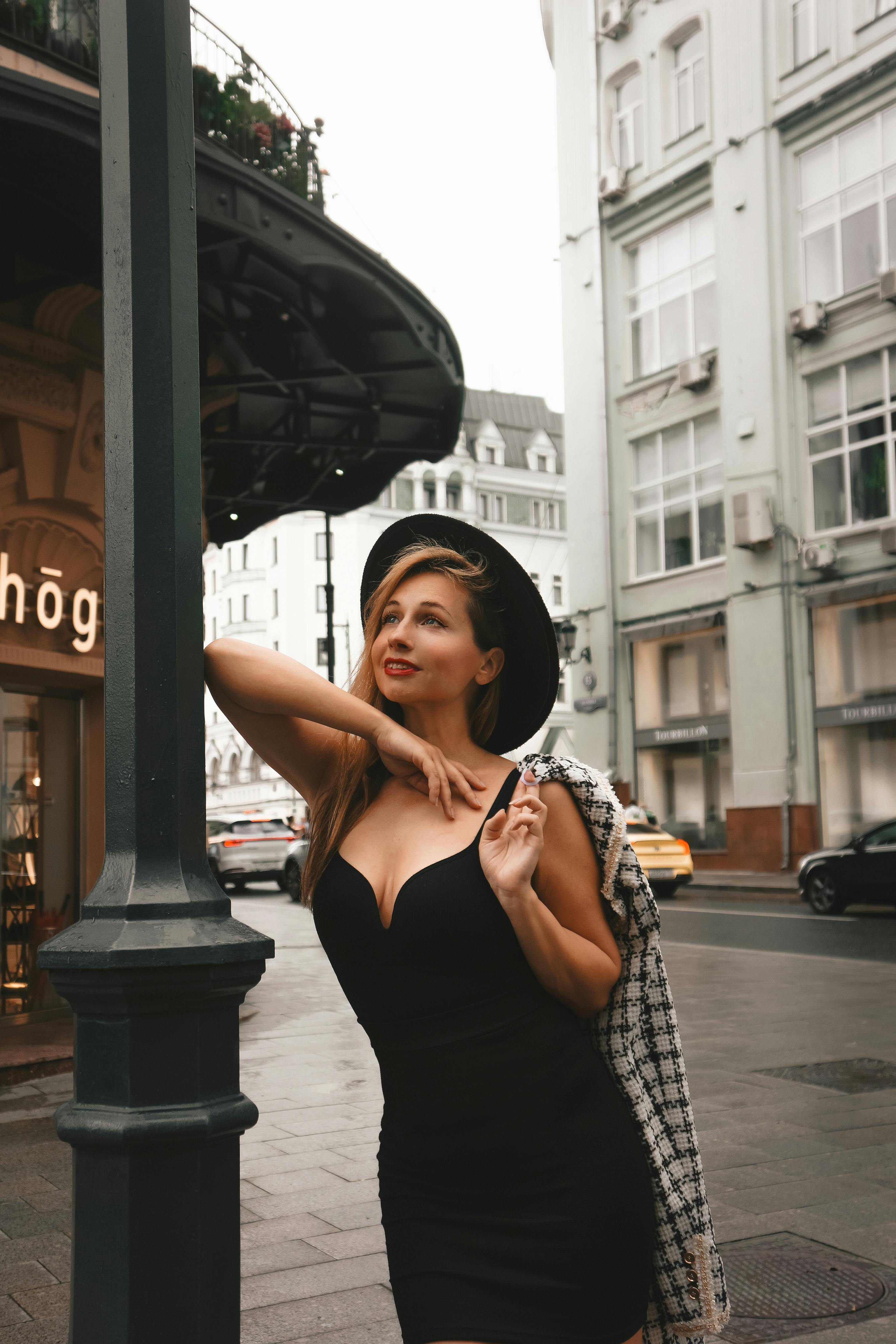 Stylish woman in a hat poses confidently on a bustling urban street, epitomizing modern city fashion.