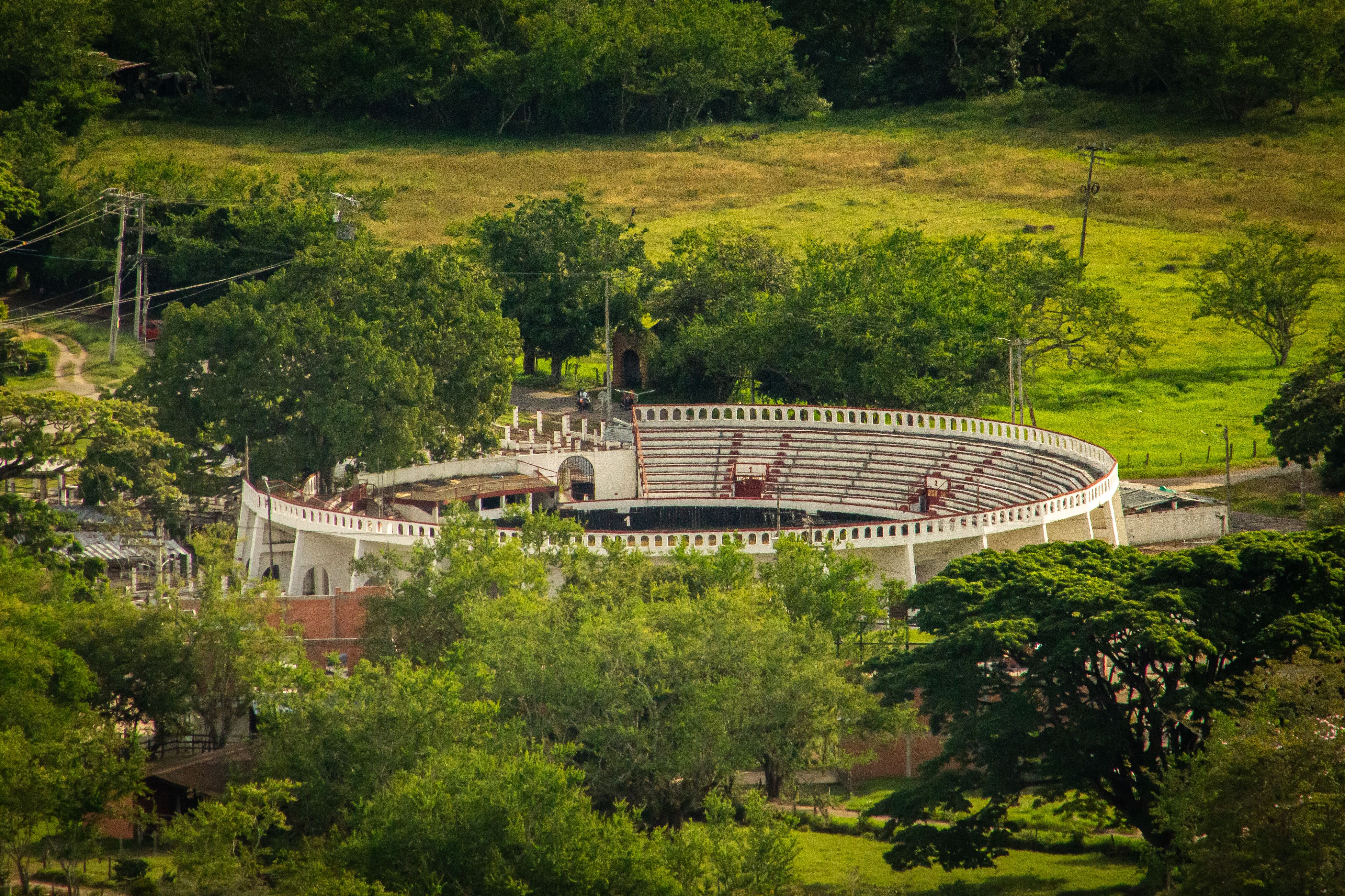 Ariel view of an old bullring encapsulated by green trees and fields under a clear sky.