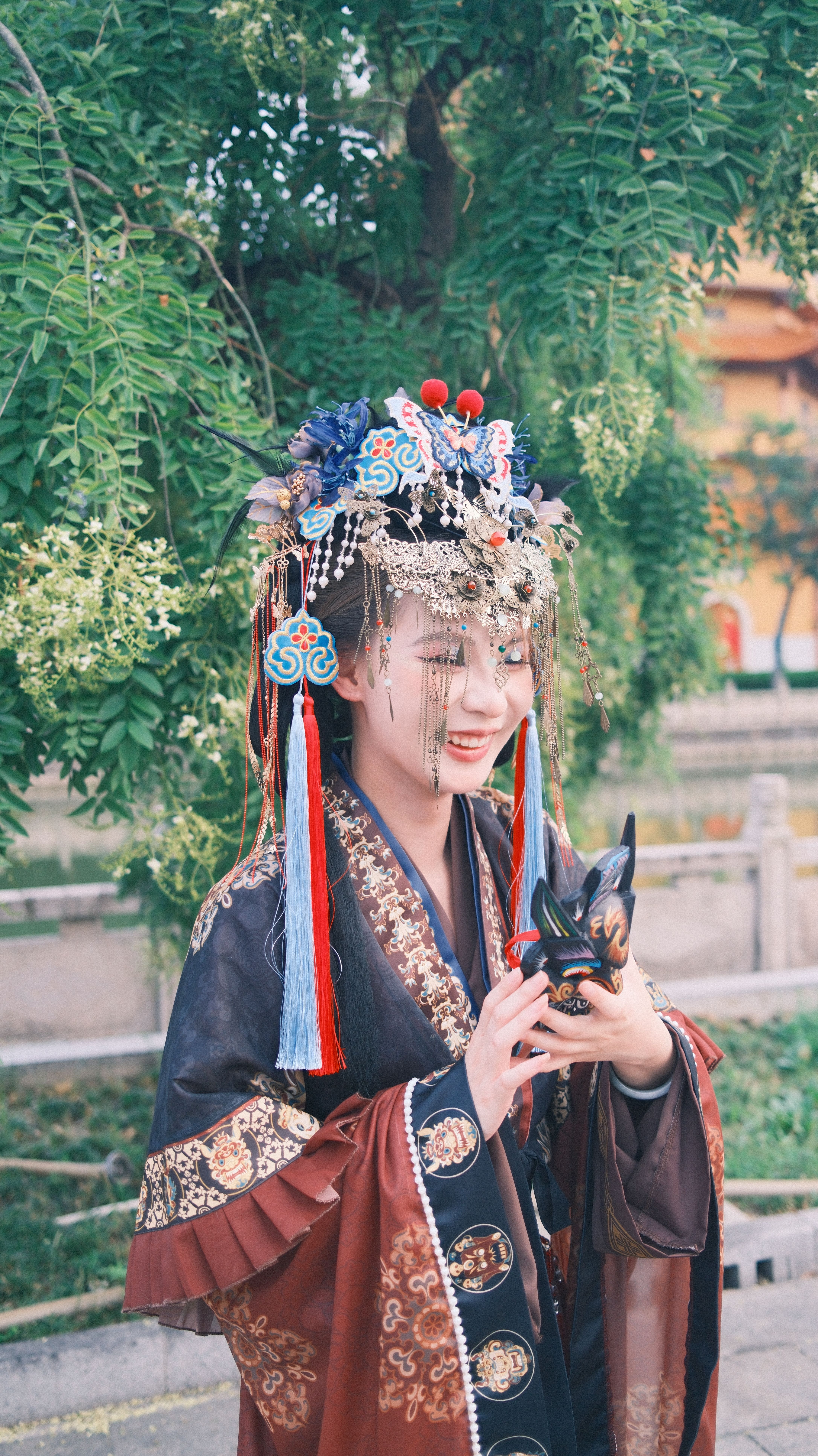 A joyful woman in ornate traditional attire poses in a lush outdoor setting.