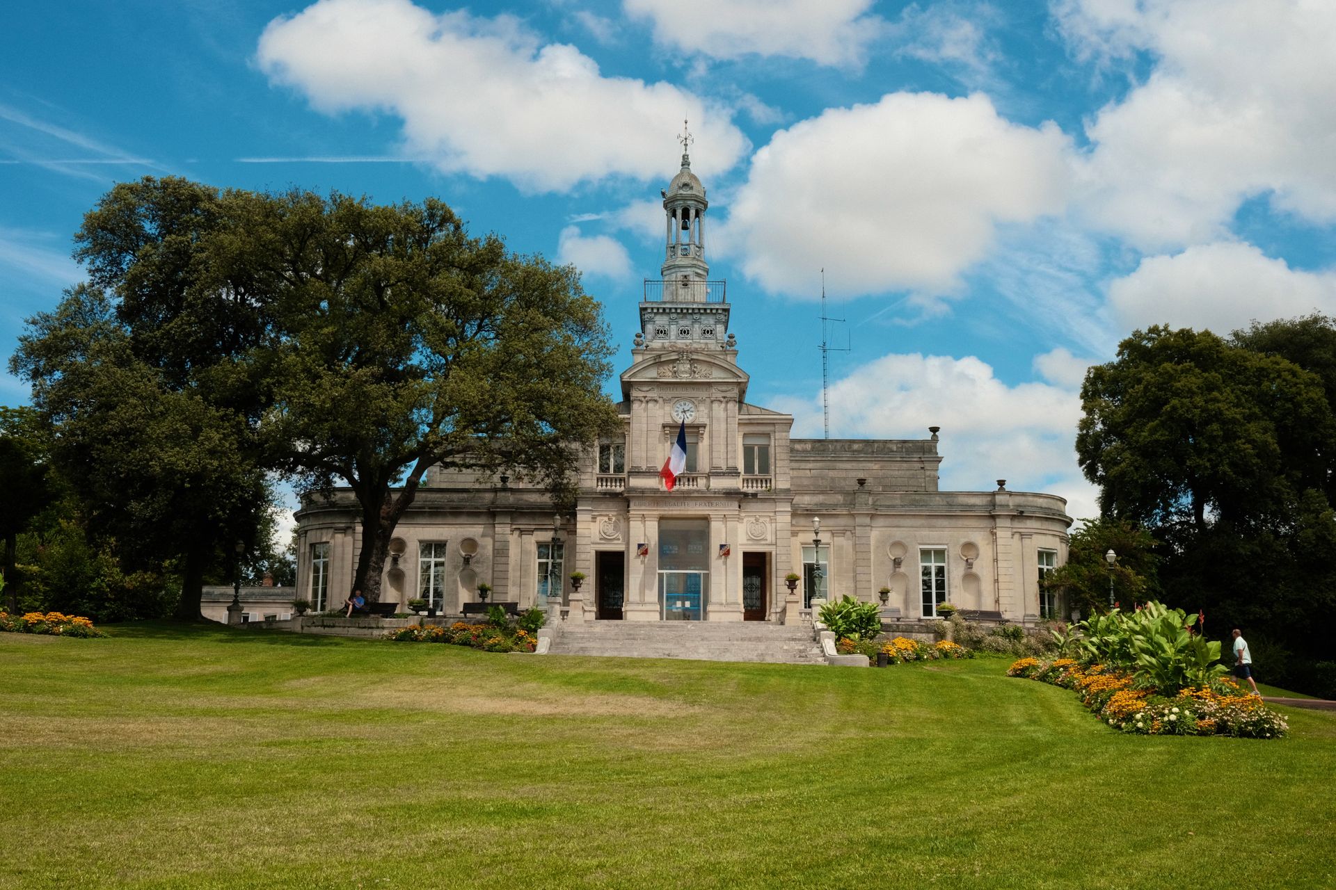 Beautiful historic building with French flag and lush gardens under a blue sky.