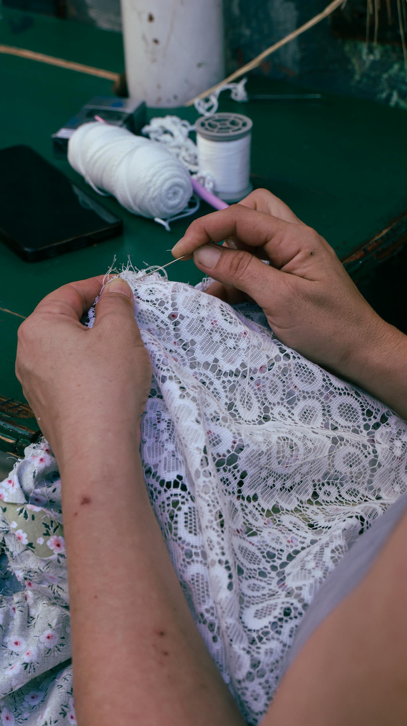 Mani che cuciono pizzo a filo su un tessuto chiaro con cura
