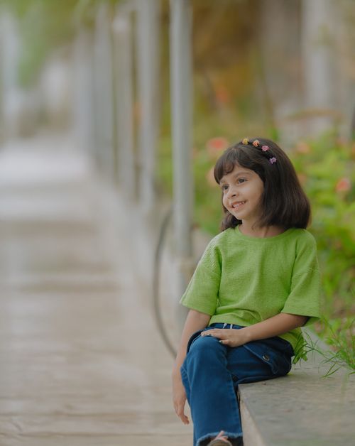 Free Smiling young girl sitting outdoors in a garden, wearing a green shirt. Stock Photo