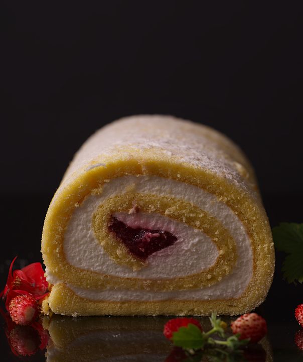 Swiss Roll Masterclass: How to Bake, Fill, and Roll Without Cracks (Eggless Version Included) 4 Professional baker slicing a Swiss roll log cleanly to reveal a perfect spiral of cream and sponge