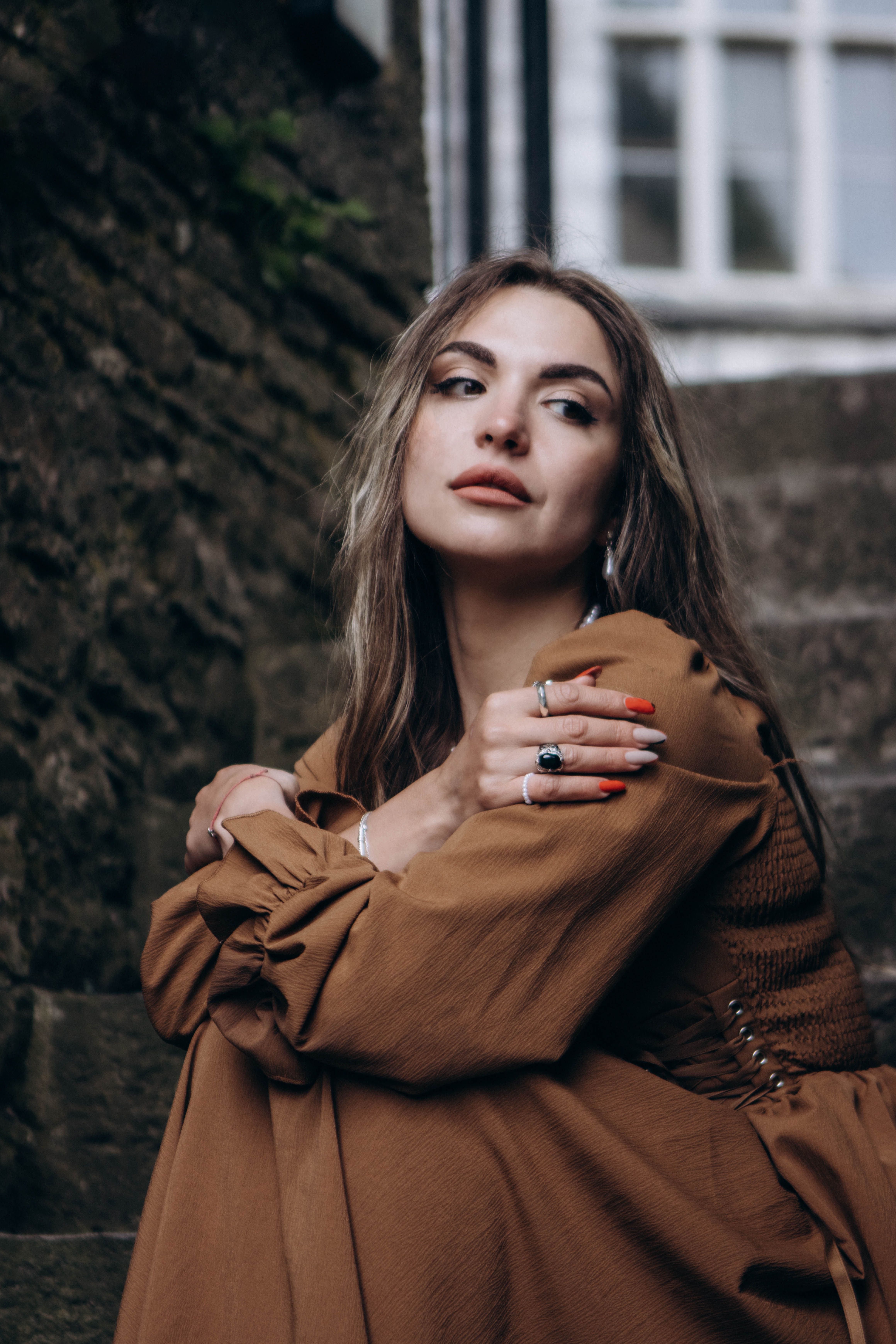 Young woman in brown dress sitting on stone stairs, thoughtful expression.