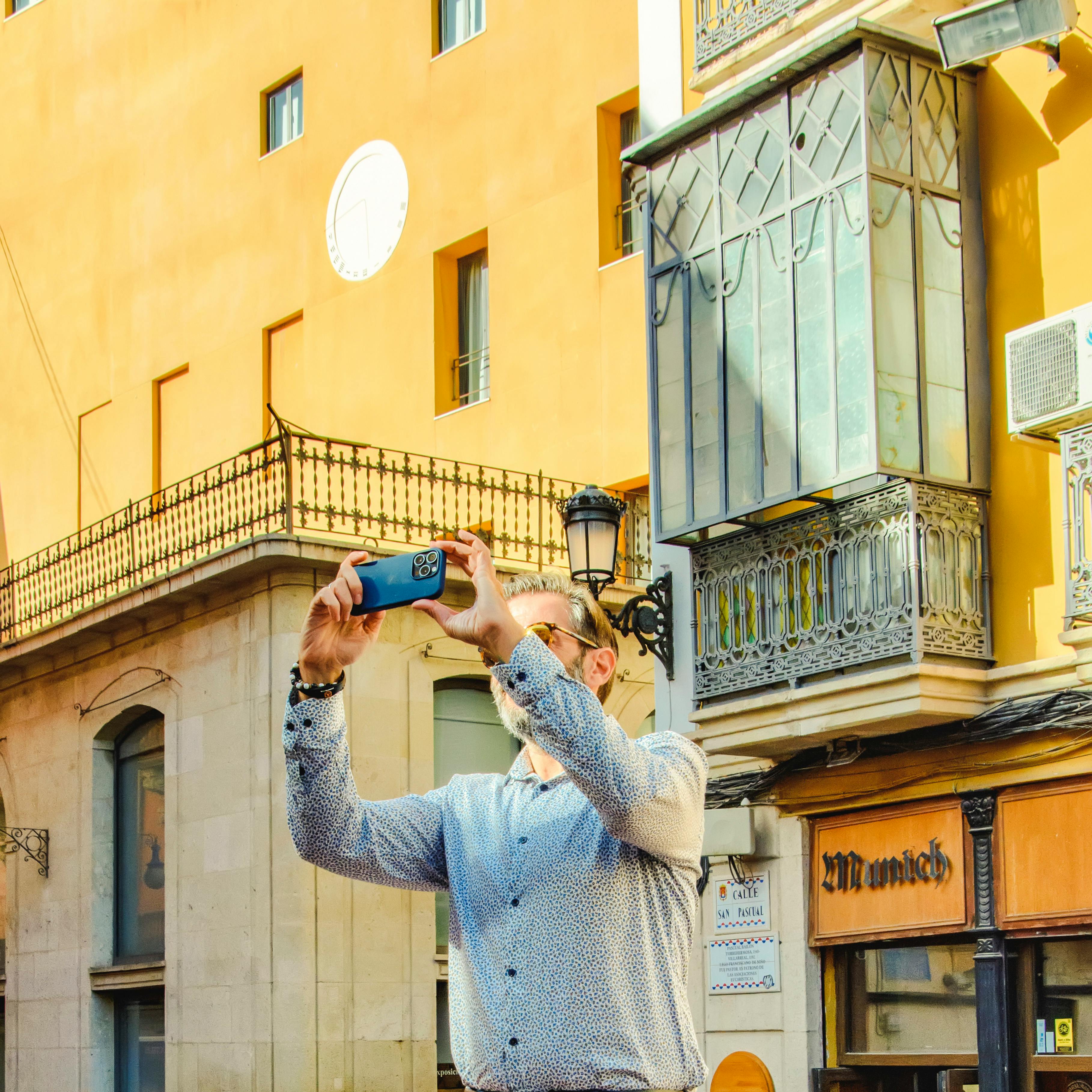 A man captures a vibrant moment in Alicante's charming old town on a sunny day.