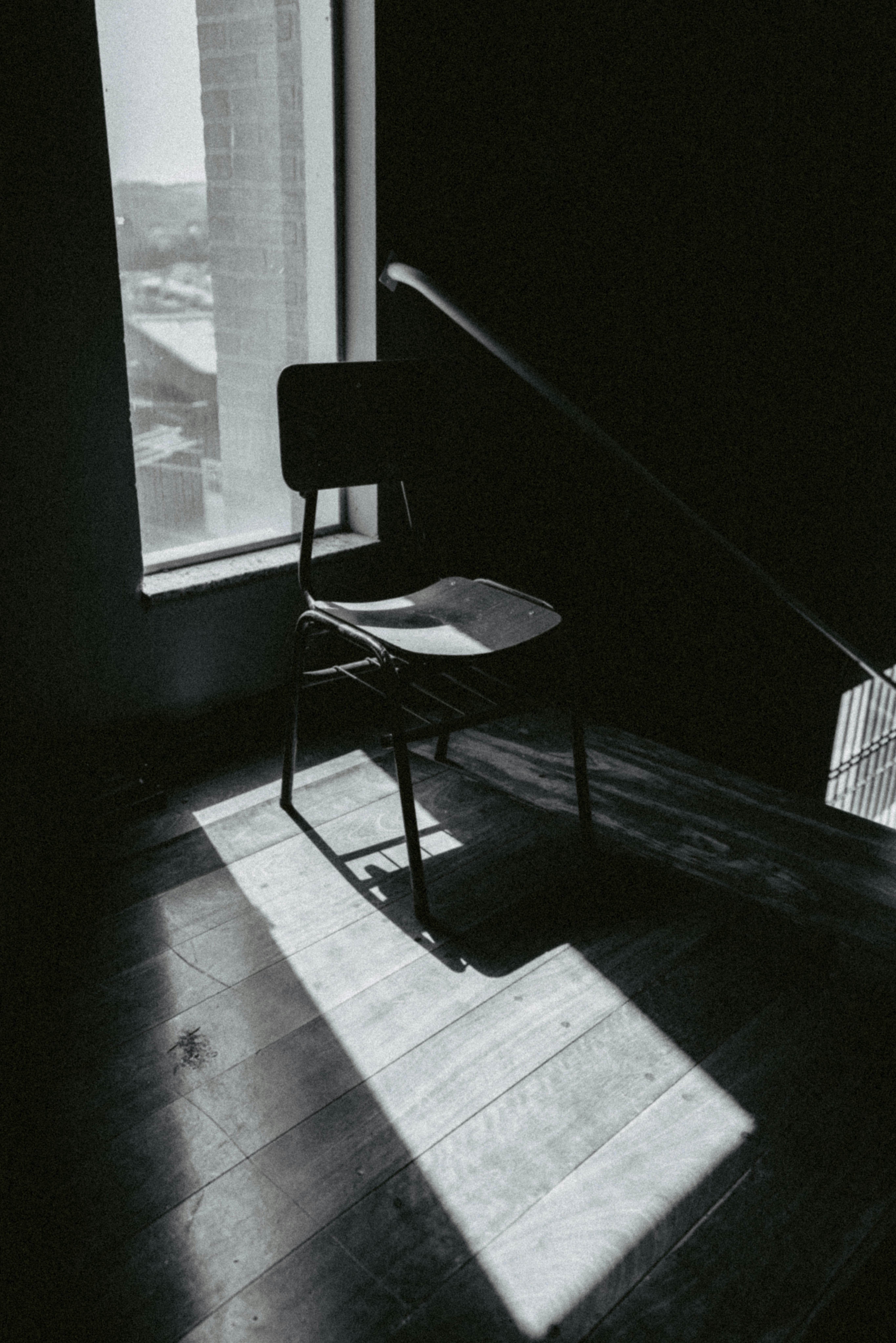 gratis Een enkele stoel in een schaduwrijk trappenhuis die dramatische licht- en schaduwpatronen werpt. Stockfoto