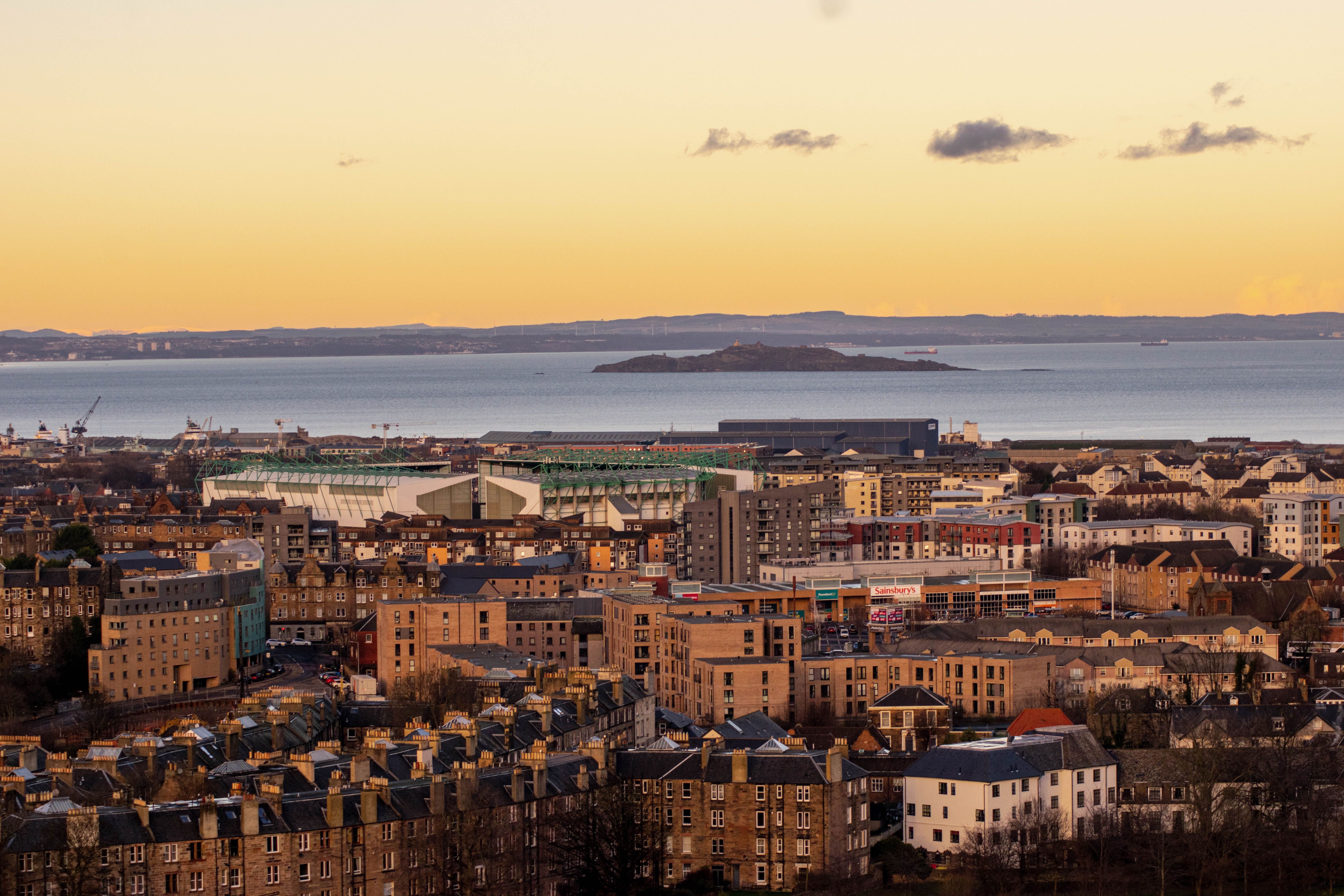 Stunning aerial view of Edinburgh skyline with coastal backdrop at sunset, capturing urban and natural beauty.