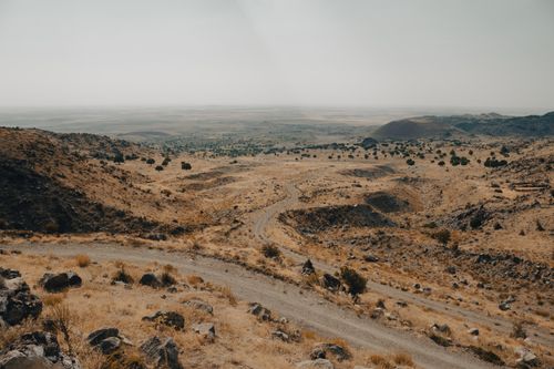 Free A winding dirt road cuts through a rugged, arid landscape with hills under a clear sky. Stock Photo