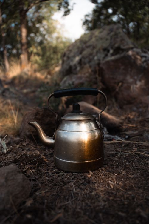 Free A weathered metal kettle placed on earthy forest ground, evoking a rustic camping vibe. Stock Photo