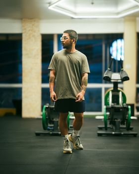 A young man in a gym setting, surrounded by fitness equipment, looking to the side.