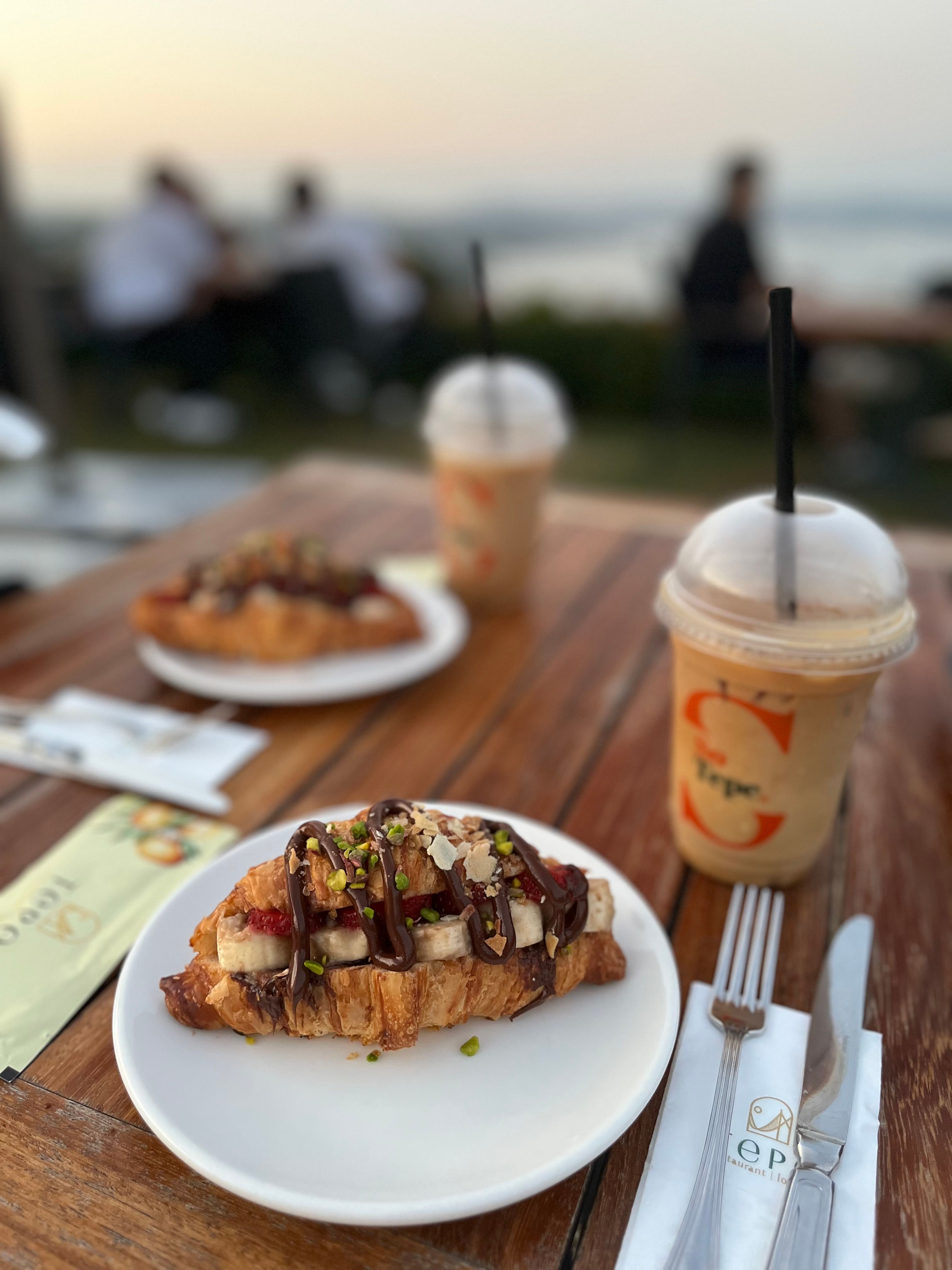 Delicious croissant and iced coffee served at an outdoor café with scenic view.