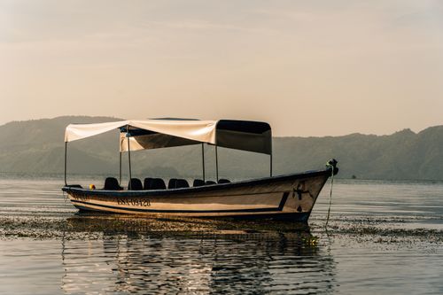 Free A tranquil boat on a calm lake with volcanic hills in the backdrop in El Salvador at dawn. Stock Photo