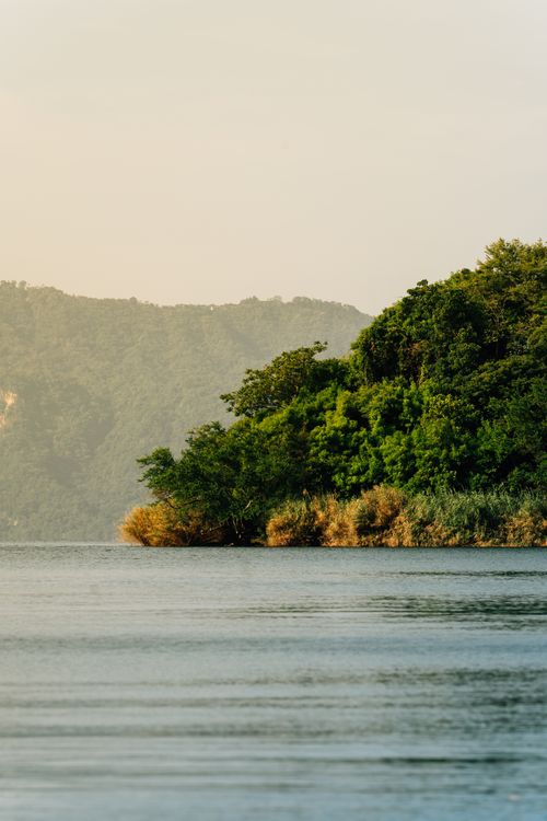 Free Tranquil morning view of a lush green hill by a calm lake in El Salvador. Stock Photo