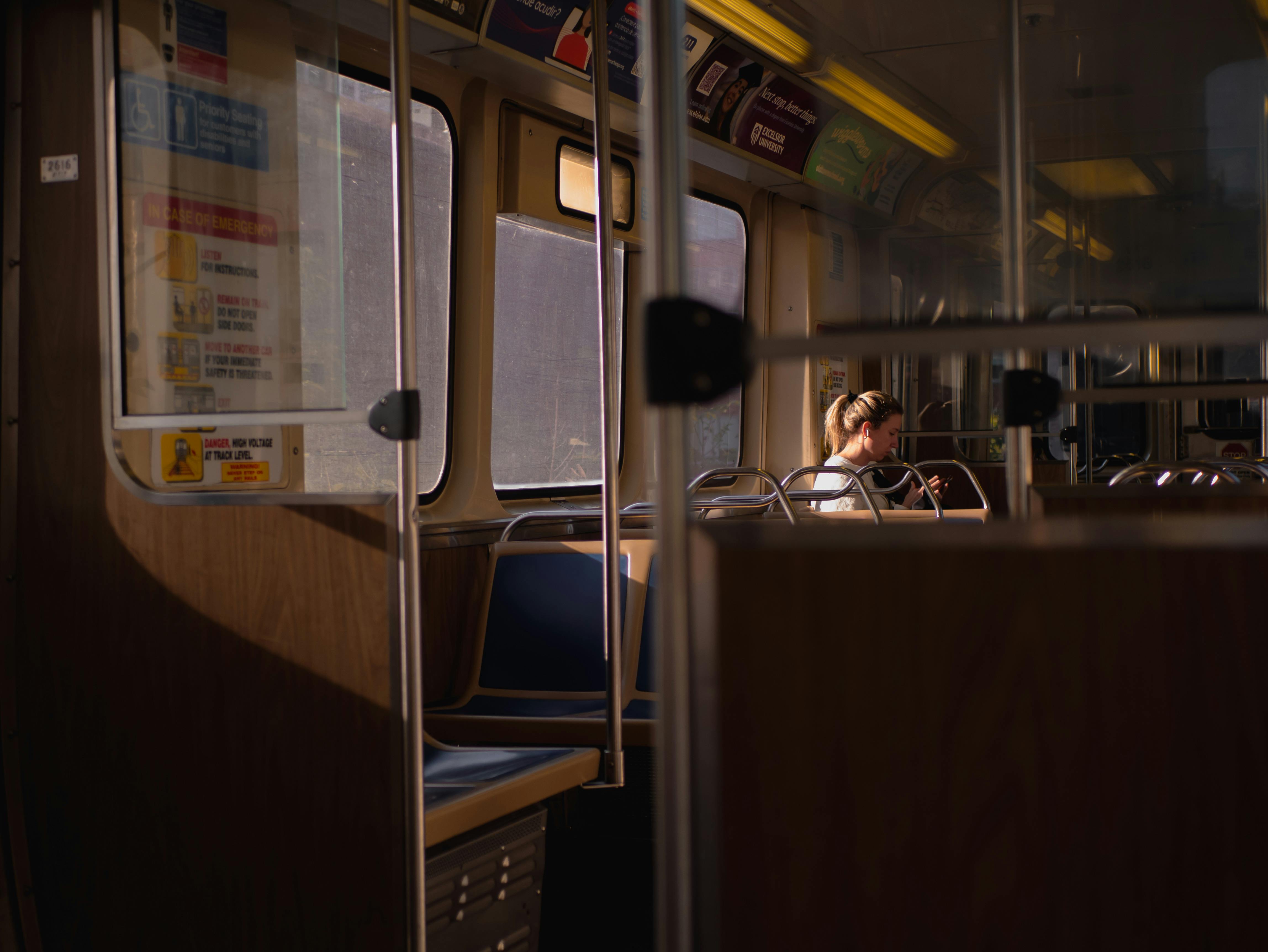 無料 一人の女性が空の電車に乗り、暖かい夕焼けの光を浴び、静かな情景を描き出しています。 写真素材