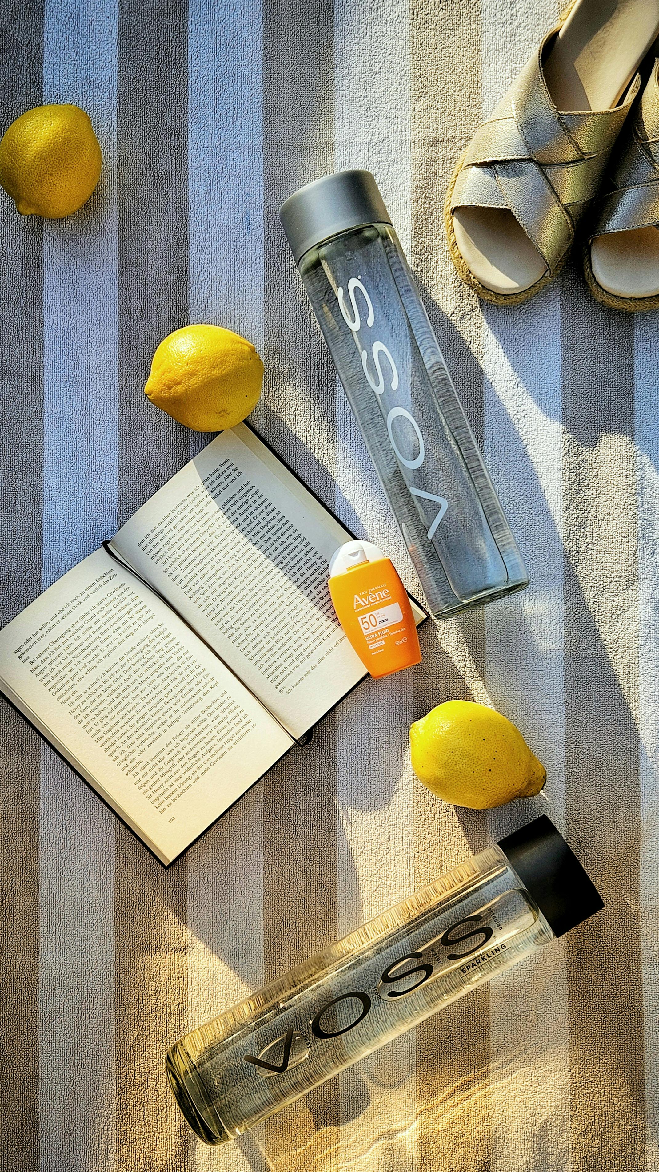 A serene summer setting with lemons, a book, and water on a striped towel.