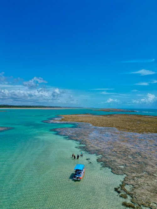 Free Stunning aerial view of clear turquoise waters, boat, and coral beach under a bright blue sky. Stock Photo