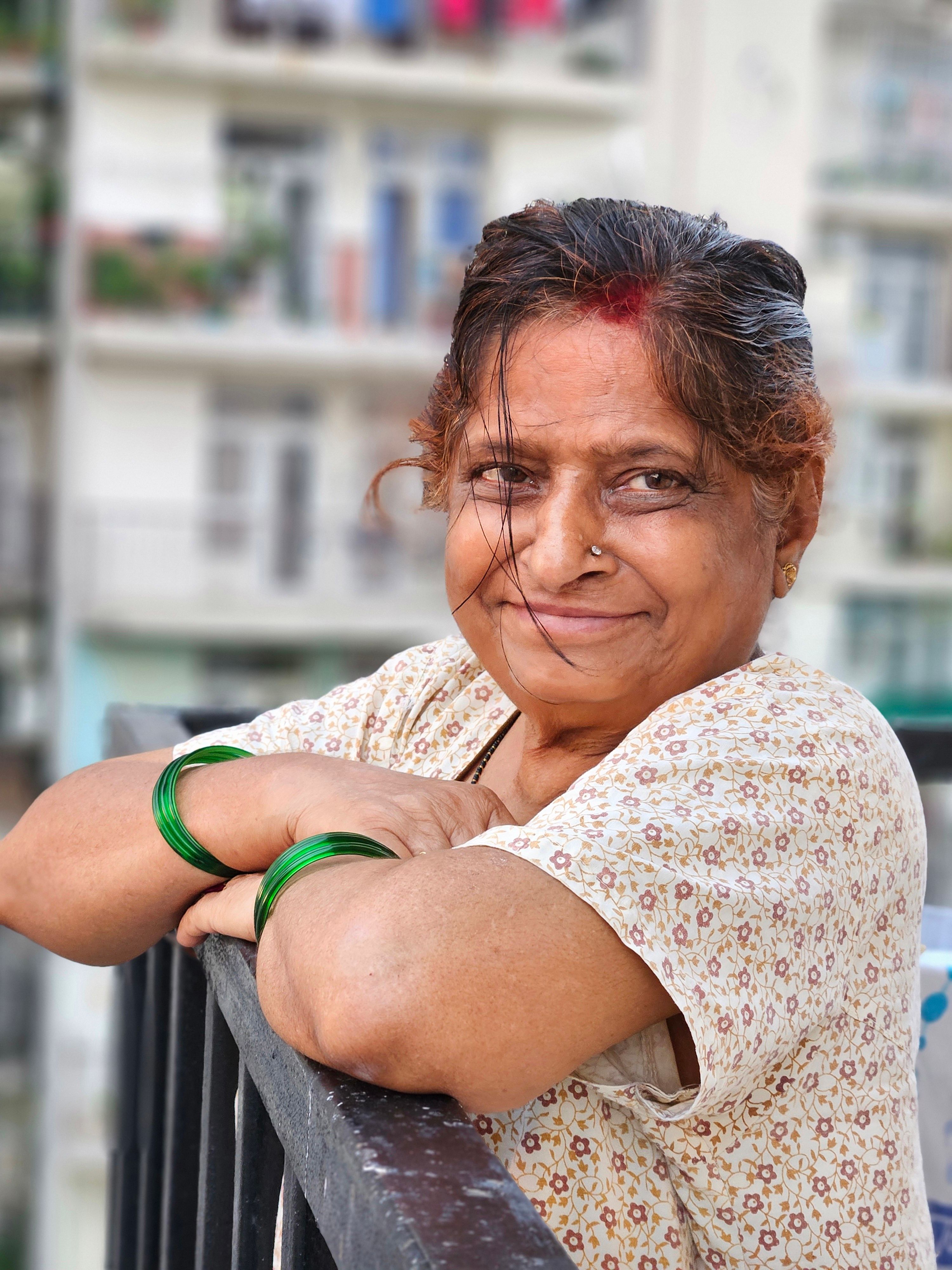 Senior woman smiling while leaning on railing on a balcony in an urban setting.