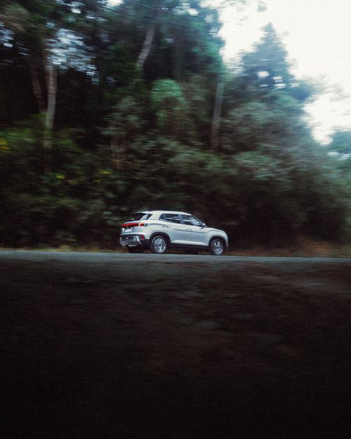 Free A silver SUV speeding along a lush, forested mountain road under a clear sky, showcasing nature's beauty. Stock Photo