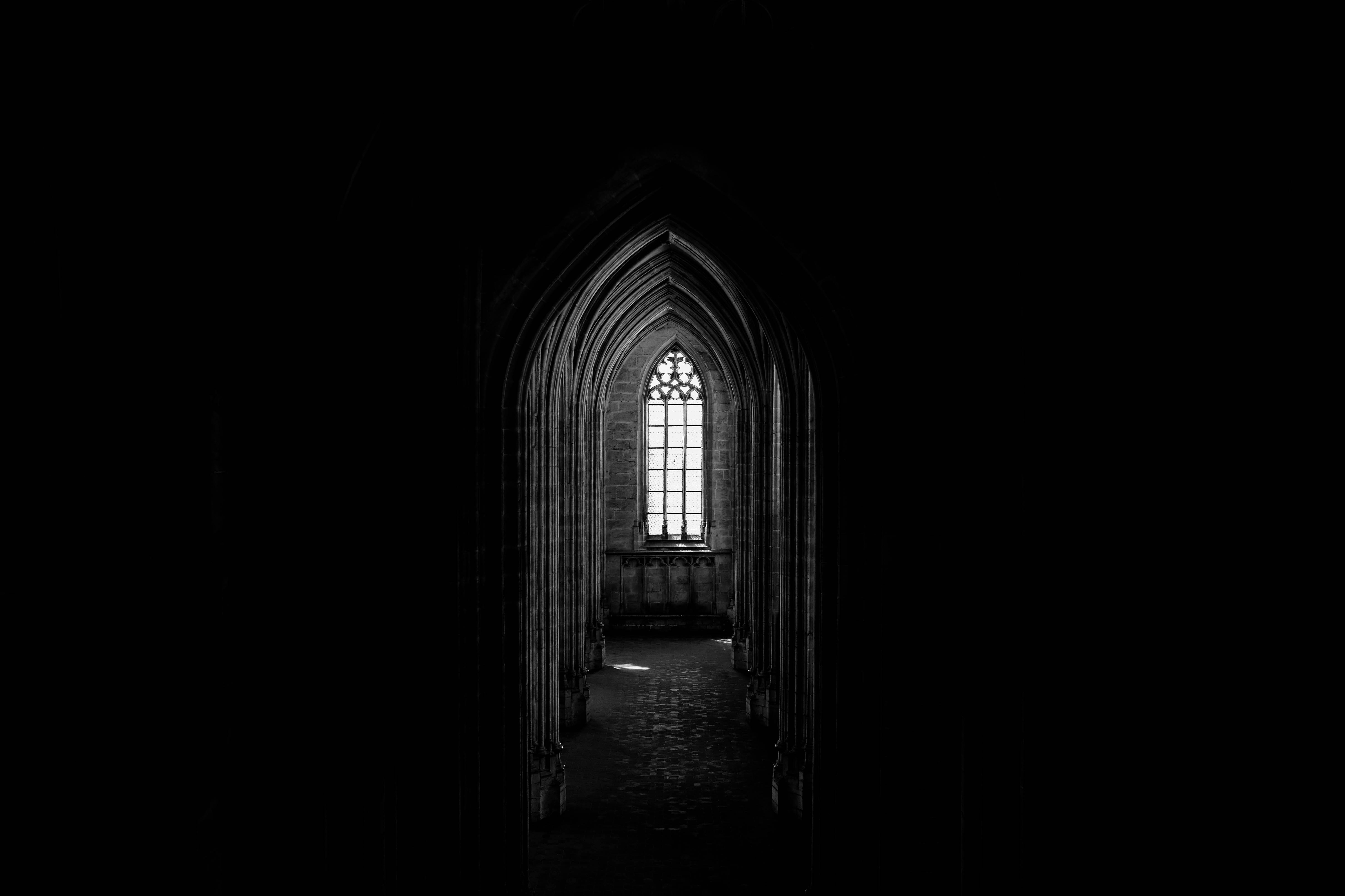 Black and white of ancient dark church with narrow corridor and arched glass window with ornament in old stone building