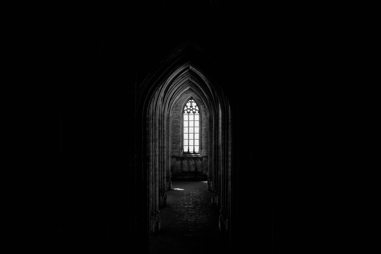 black and white of ancient dark church with narrow corridor and arched