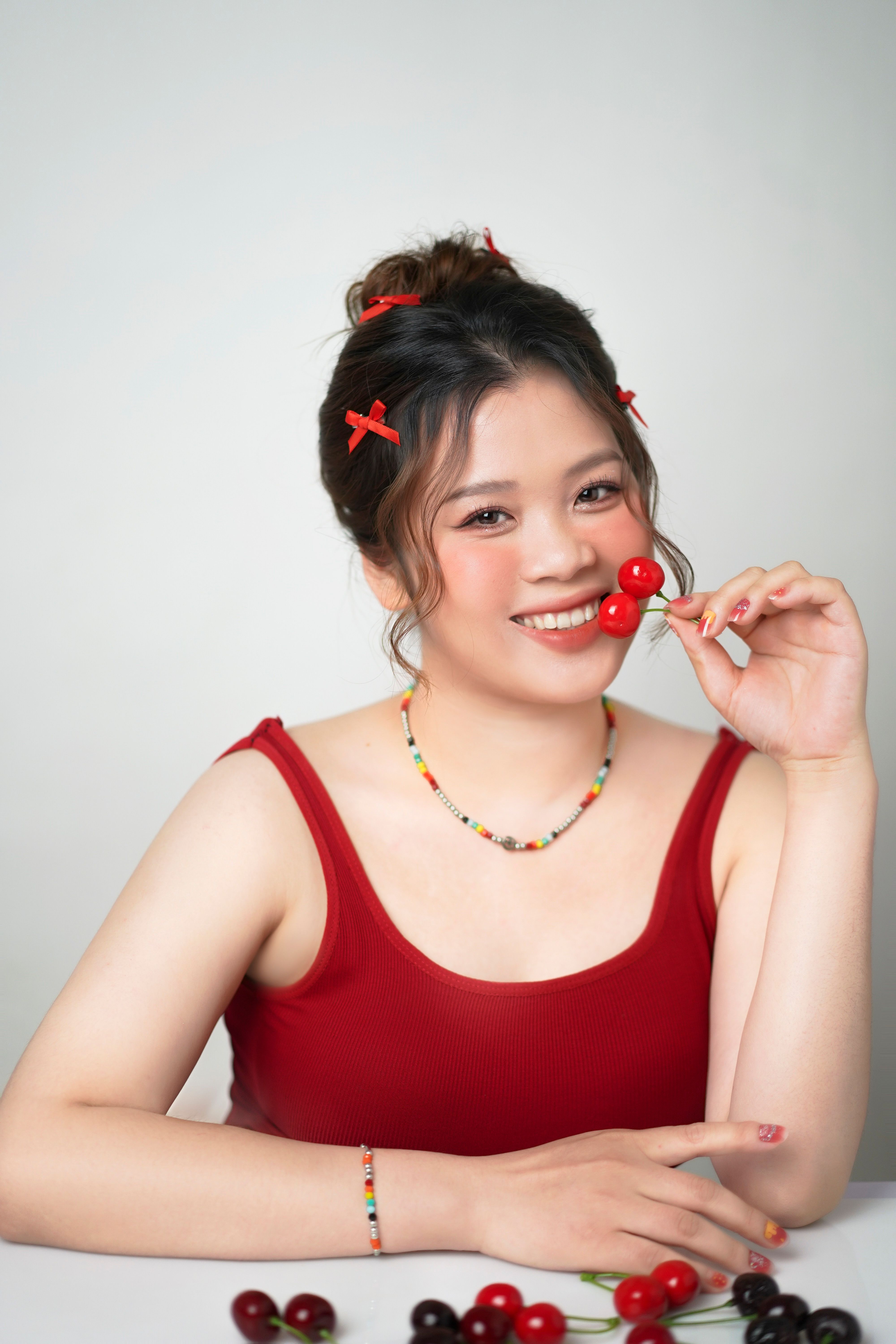 Smiling woman in red outfit enjoying fresh cherries indoors.