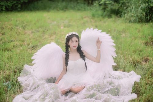 Free A serene image of a woman in angelic attire sitting gracefully on a lush meadow. Stock Photo