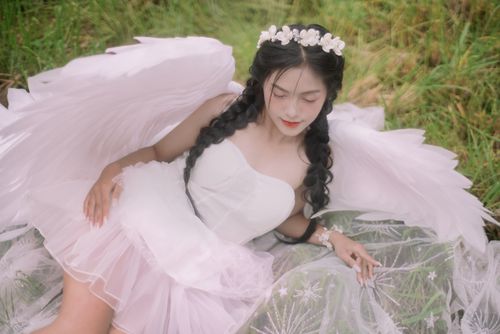 Free Serene woman in angel wings lying in grass, exuding ethereal beauty. Stock Photo