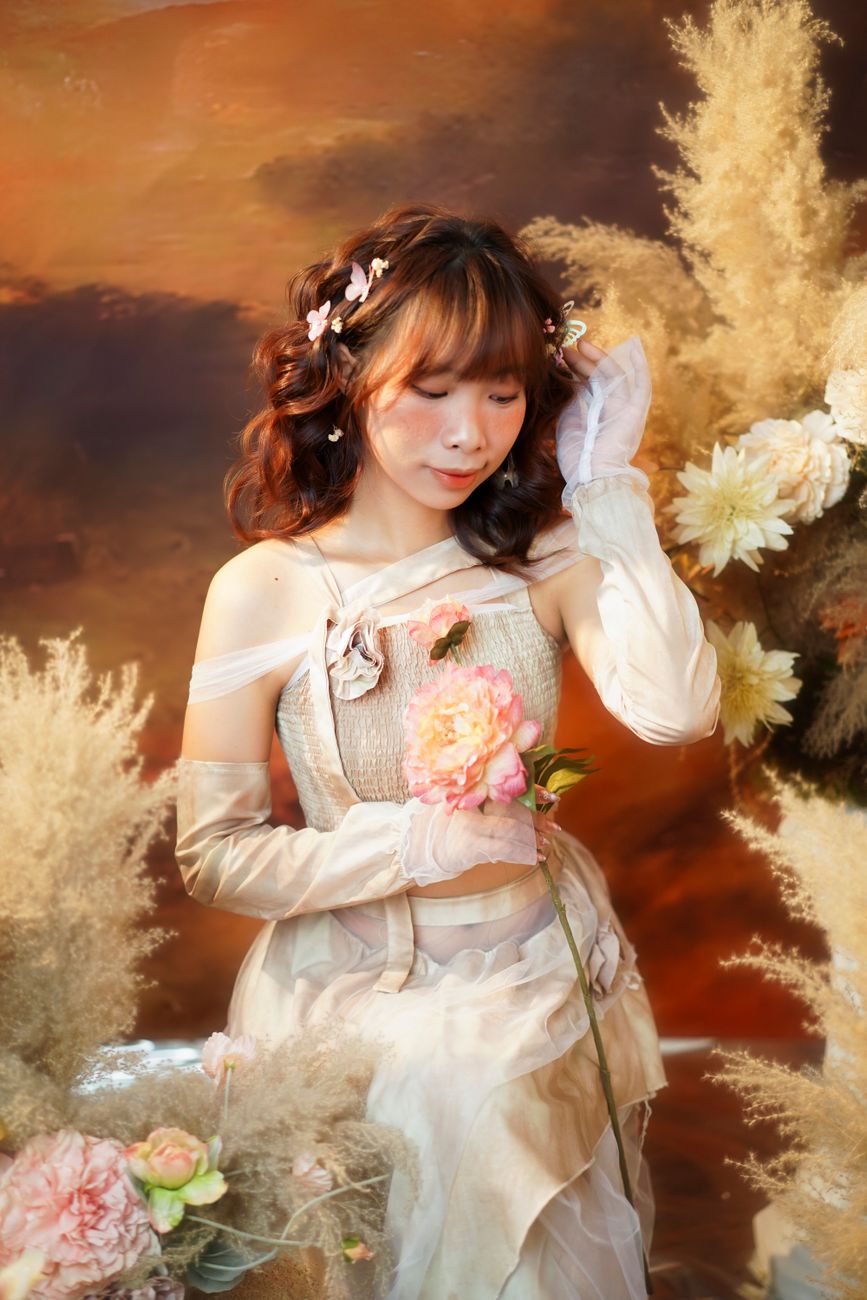 Elegant portrait of a woman in a vintage dress holding flowers, surrounded by pampas grass with a warm background.