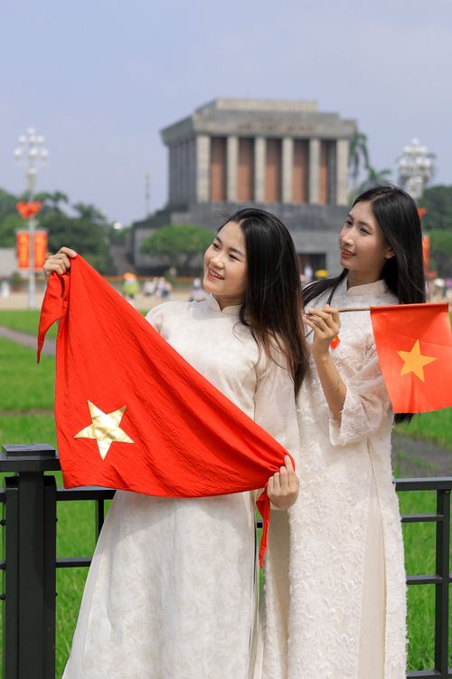 Free Two women in traditional ao dai holding Vietnam flags at Ho Chi Minh Mausoleum. Stock Photo