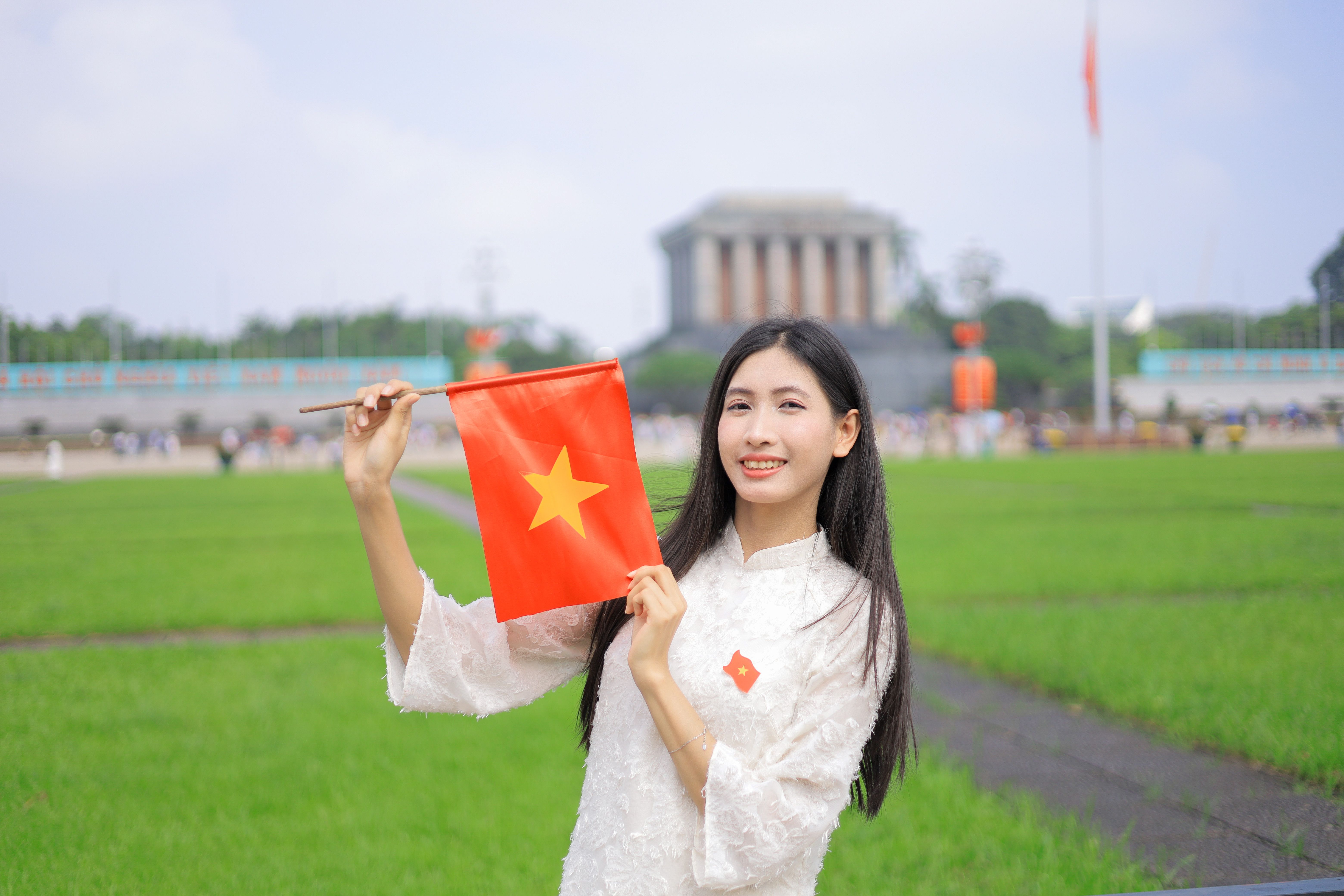 Cheerful woman in Vietnamese ao dai holding Vietnam flag at a famous landmark.