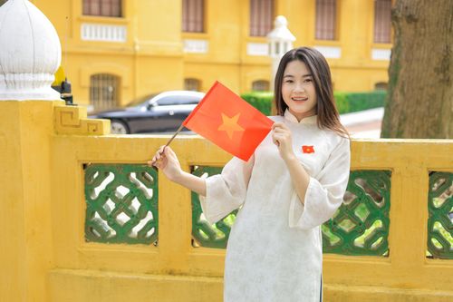 Free Woman in traditional Ao Dai with Vietnamese flag outdoors, exuding patriotic pride. Stock Photo