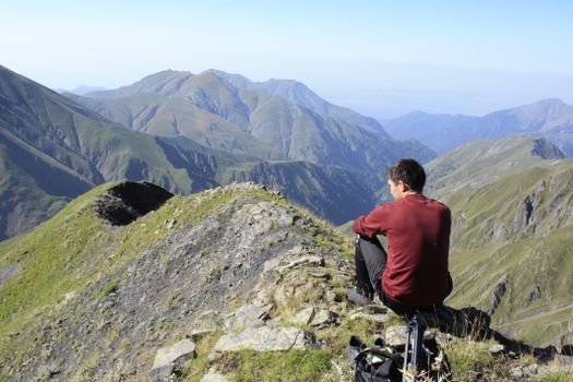 A man sits on a mountain ridge enjoying breathtaking natural views.