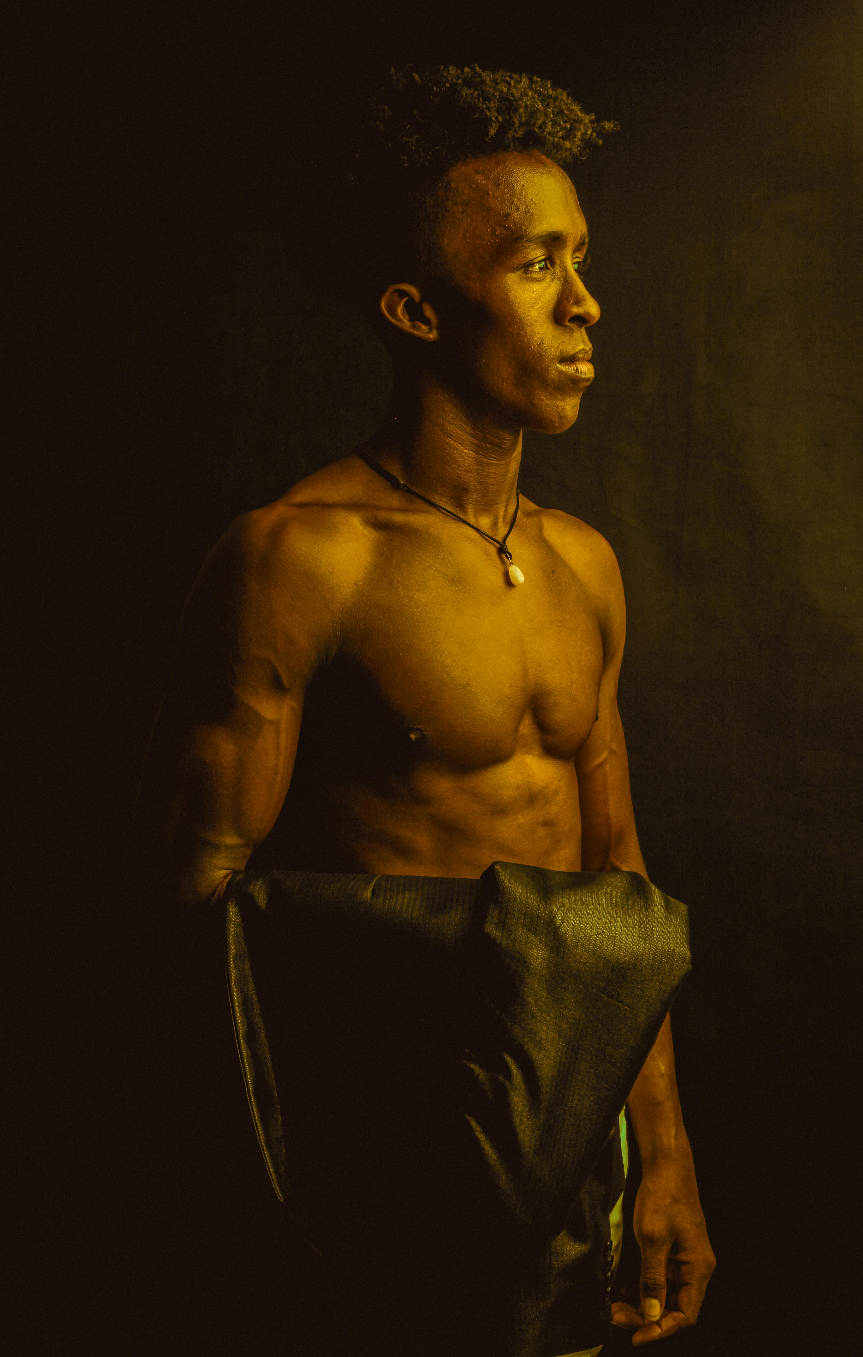 Gratuit Portret dramatic al unui bărbat musculos, evidențiat de o lumină caldă, de bronz, demonstrând forță și măiestrie artistică. Fotografie de stoc