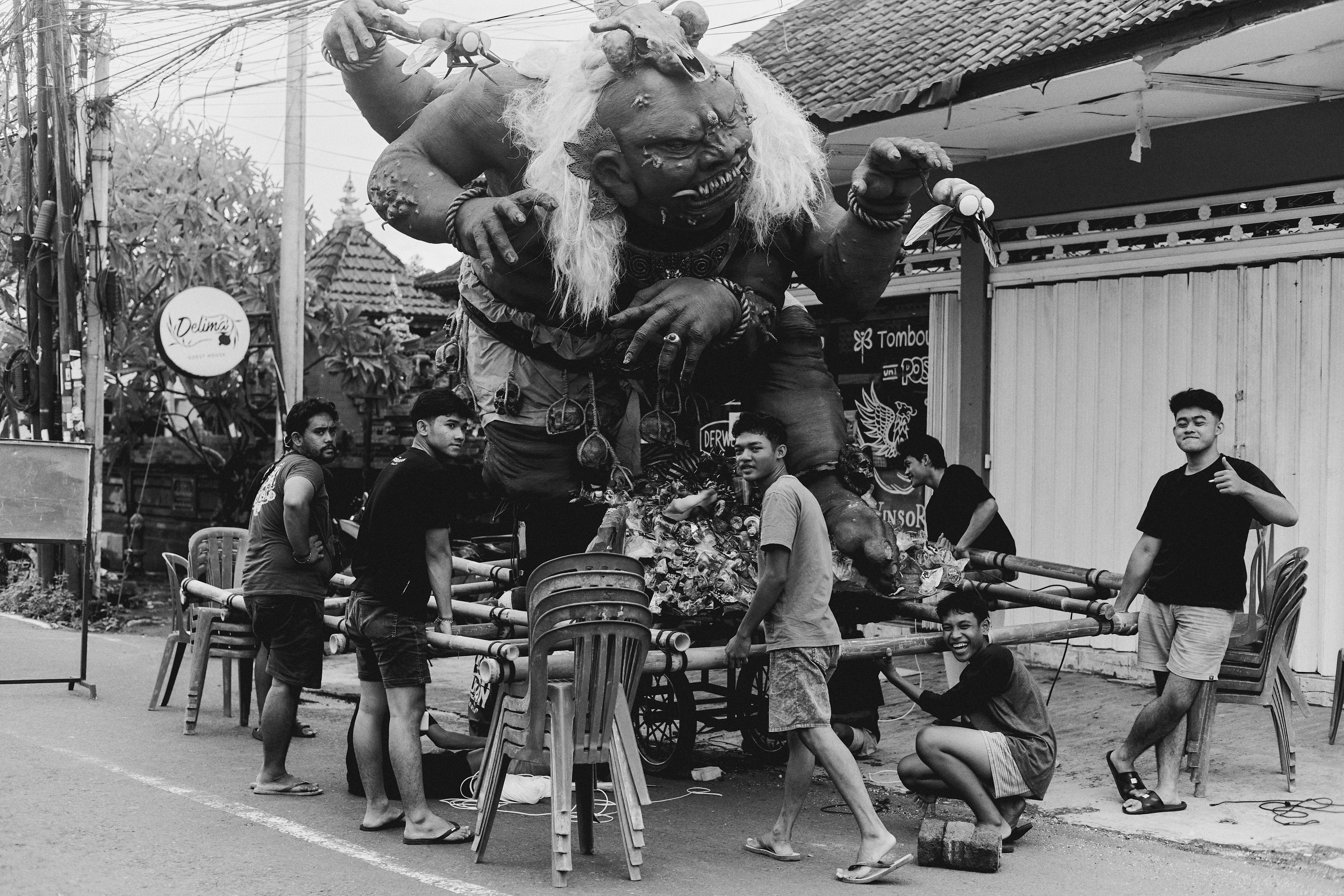Ogoh-ogoh displayed with a group of young adults during a parade preparation in Bali. Captured in black and white.