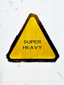 Yellow triangle sign indicating 'Super Heavy' caution on white wall.