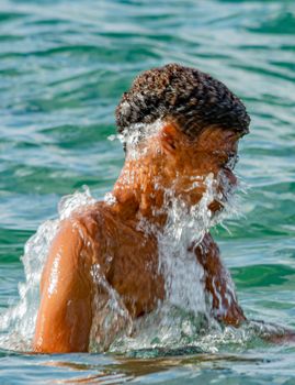 A young man enjoys a refreshing splash in clear ocean water on a sunny day.
