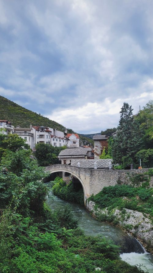 Free Picturesque view of an old stone bridge in a lush, green landscape near urban Bosnian scenery, captured during the day. Stock Photo