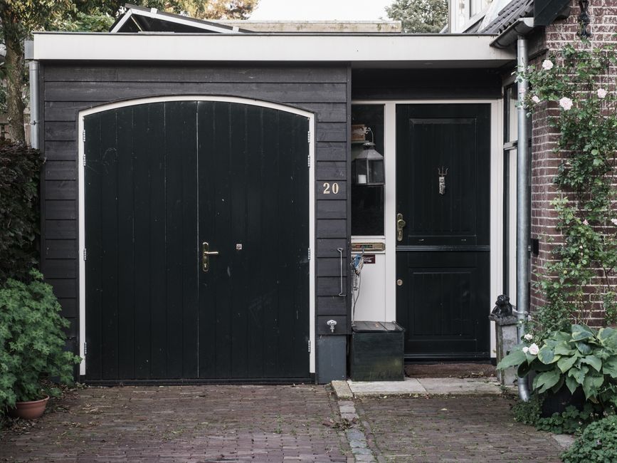 Exterior of a traditional Dutch house with black doors and a landscaped garden.