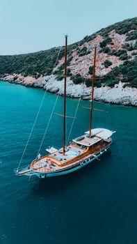 Aerial view of a sailboat moored near a lush, rocky coastline with clear blue waters.