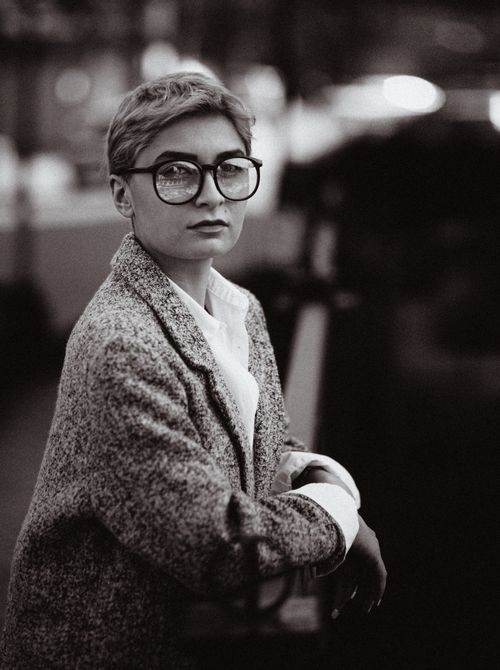 Free Elegant black and white portrait of a woman in glasses with a stylish coat in urban setting. Stock Photo