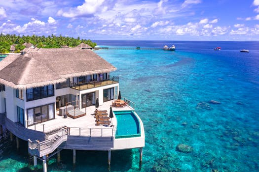 Aerial view of a luxurious overwater villa with infinity pool in a tropical resort, surrounded by clear blue ocean.
