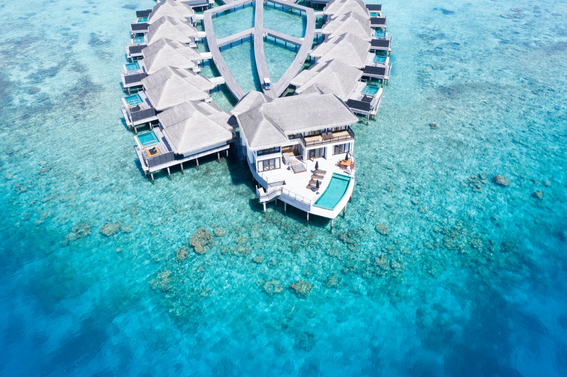 Drone shot of luxury overwater resort villas with reef and channels visible for planning water villa booking advice