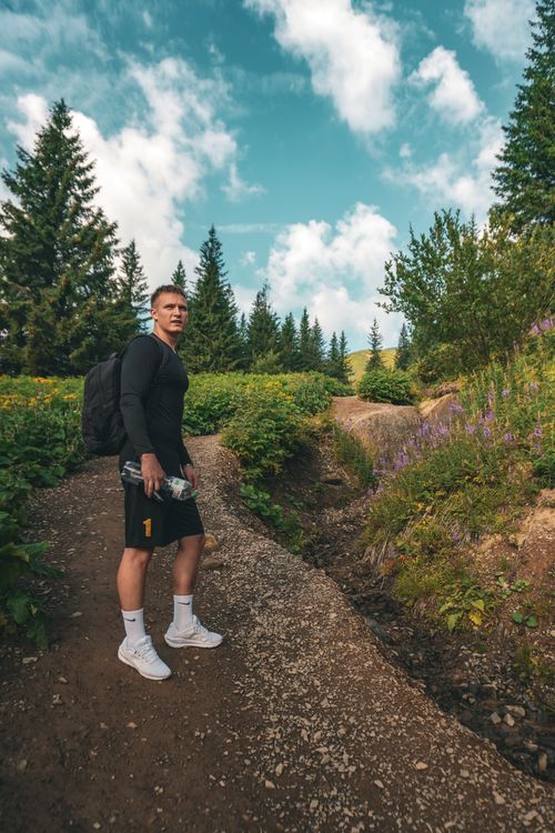 Free Man hiking on a lush mountain trail with a backpack under a clear sky. Stock Photo